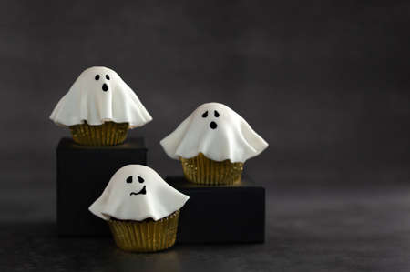 Halloween fondant ghost cupcakes on black podiums. Halloween party food idea.