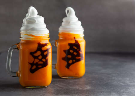 Halloween Pumpkin cocktail with whipped cream in ghost shape and chocolate spider web. Freakshake for party.の写真素材