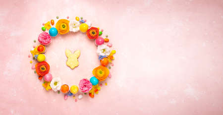 Easter eggs, cookie and colorful spring flowers made in shape of circle wreath on pastel pink...