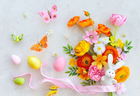 Holiday concept with bouquet of spring flowers, Easter eggs, bunny and butterfly on pastel vintage background. Easter composition, flat lay.の写真素材