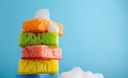 Household Cleaning Scrub Colored Sponges with soap foam. Kitchen Dishwashing Sponge on blue...