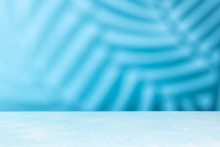 Blue table top with shadow of palm tree leaf on blue wall background. Abstract summer backdrop with copy space.Palm coconut leaf shadowの写真素材