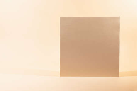 Gold Paper sheet or blank card on beige background. Creative background with empty sheet of paper...