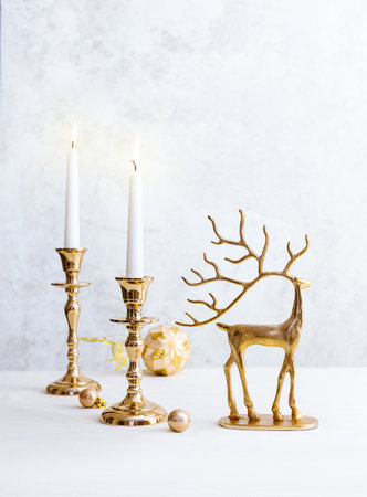 Festive still life with burning candles, figure of deer and Christmas decorations on pastel light background. Christmas composition for home interiorの写真素材
