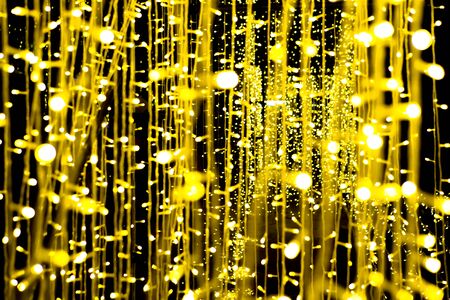 Light bulb hanging a chandelier, illuminating a small, beautiful yellow gold bokeh on a black...