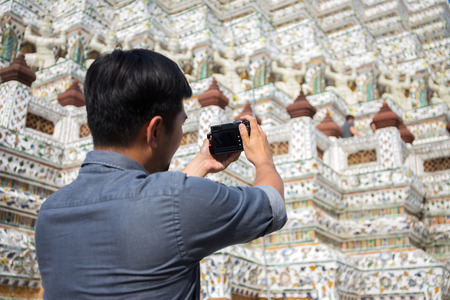 Back view of a young man tourist taking photo of famous temple in thailand, Hobby and travel conceptの写真素材