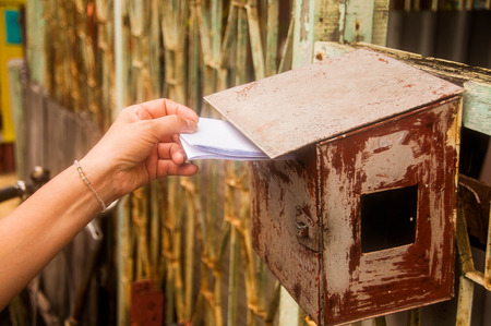 closeup on a female hand putting a letter in a letterboxの写真素材