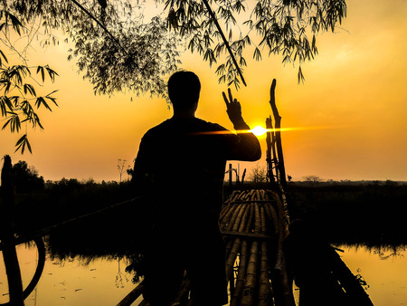 Man with peace sign on the bamboo bridge over the river,silhouette styleの写真素材