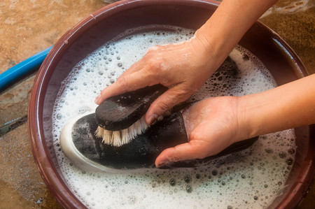 Woman hand cleaning black shoes or sneaker by wooden brush and soapsuds on bowlの写真素材