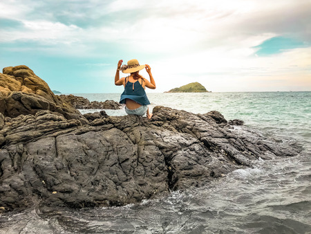 woman tourist sitting on the stone reef off the coast with Sea waves splashing and blue skyの写真素材