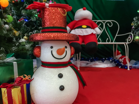 Small snow man and santa near pine tree and gift box on red floor.の写真素材
