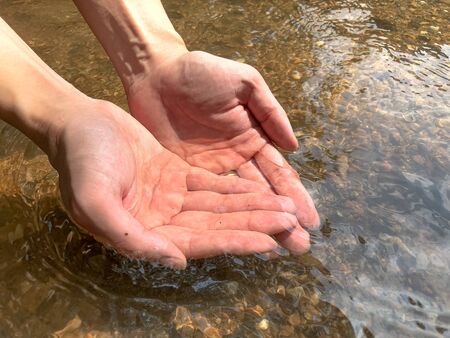 Woman catches running water in her cupped hands at waterfall.の写真素材