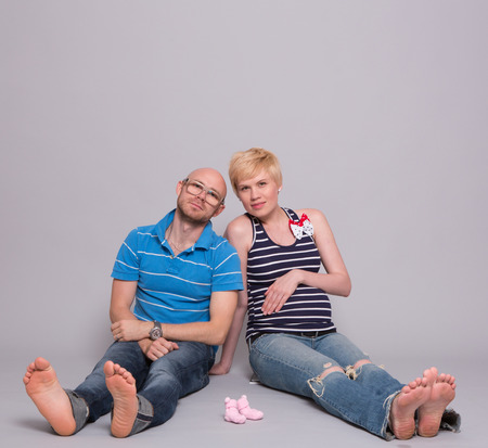 Young attractive couple pregnant mother and happy father holds a pink socks for his daughter over gray backgroundの写真素材