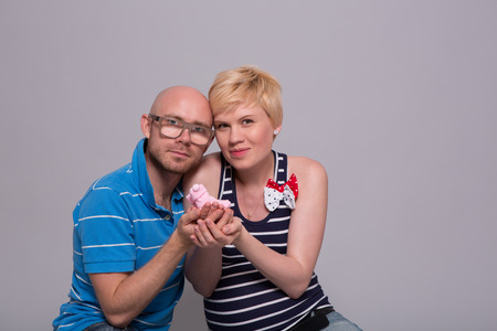 Young attractive couple pregnant mother and happy father holds a pink socks for his daughter over gray backgroundの写真素材