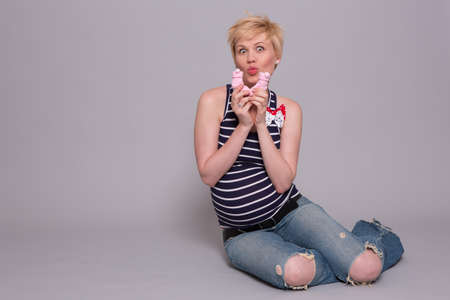 happy young pregnant woman holds a pink socks for his daughter over gray backgroundの写真素材