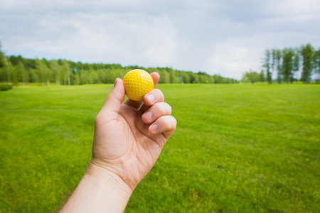 Hand with yellow golf ball over a golf courseの写真素材