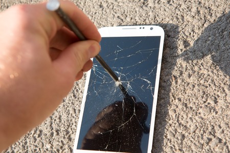 metal nail and smartphone with a broken screen over the stone surfaceの写真素材