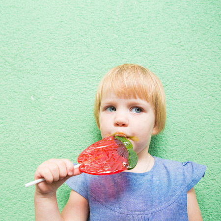 Beautiful little girl holding a big strawberry shaped lollipopの写真素材