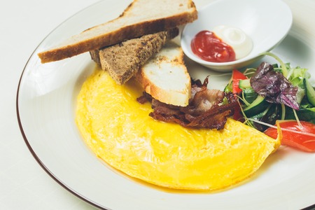 Omelet with bacon served on white plate, vegetables aside. Warm colors. Shallow dof.の写真素材