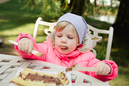 Child eating waffles with chocolate in a spring parkの写真素材