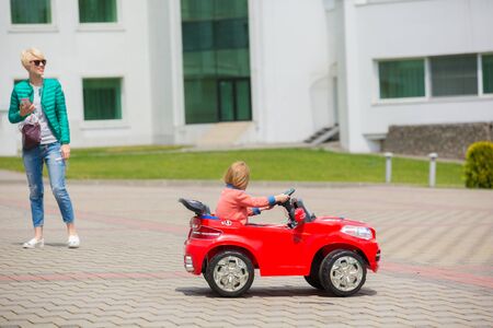 Beautiful little girl riding toy car in summer city park.の写真素材