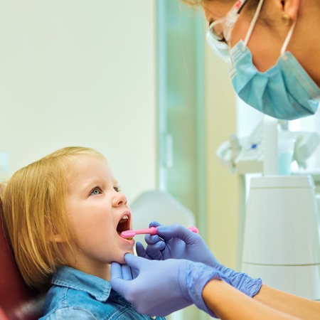 Little patient at the dentist office. The dentist brushes teeth to the little girlの写真素材