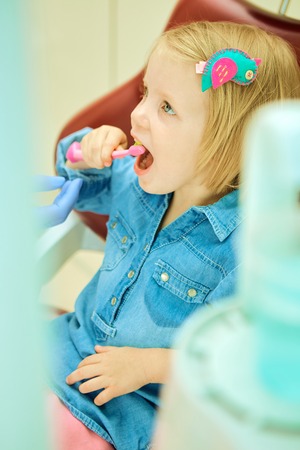 Little girl sitting in the dentists office brushes teethの写真素材