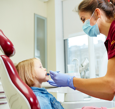 Pediatric dentist examining little girls teeth in the dentists chair at the dental clinicの写真素材