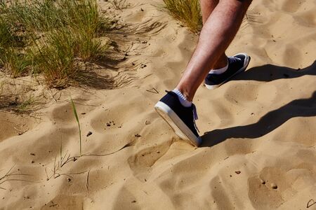 Close up fashion image of man walking alone at tropical exotic beach with blue ocean and white sand, wearing stylish sneakers.の写真素材