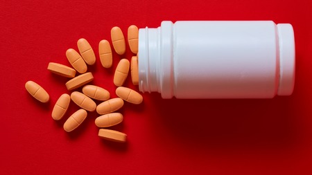 Pills spilling out of pill bottle on red. Top view with copy space. Medicine concept. Shallow dofの写真素材