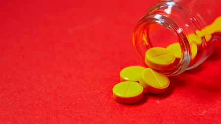 Pills spilling out of pill bottle on red. Top view with copy space. Medicine concept