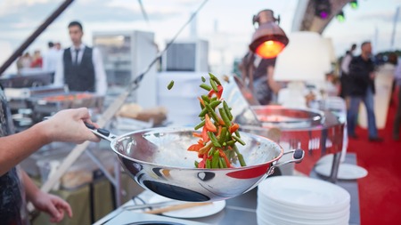chef tossing vegetables in a wok in an outdoor kitchenの写真素材