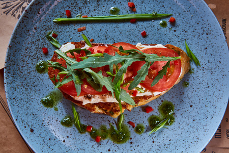 Bruschetta with cottage cheese, tomatoes and arugula served on blue creamic plate.の写真素材