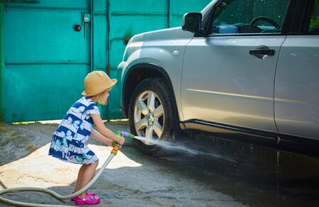 little girl spraying a car with a water hose in a sunny afternoon, rubber hose, pour water on overの写真素材