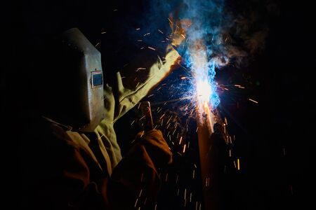 welder worker welding metal by electrode with bright electric arc and sparks during manufacture of metal equipmentの写真素材