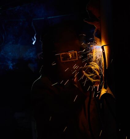 welder worker welding metal by electrode with bright electric arc and sparks during manufacture of...