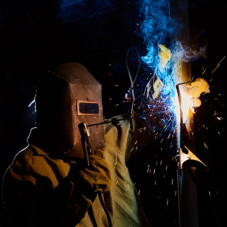 welder worker welding metal by electrode with bright electric arc and sparks during manufacture of metal equipmentの写真素材