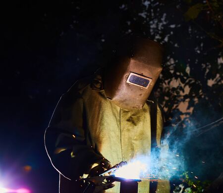 welder worker welding metal by electrode with bright electric arc and sparks during manufacture of...
