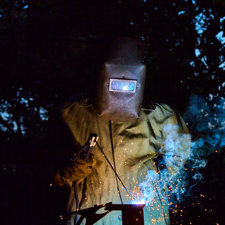 welder worker welding metal by electrode with bright electric arc and sparks during manufacture of...