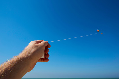 Male hand holding kite strings with a kite in sky.の写真素材