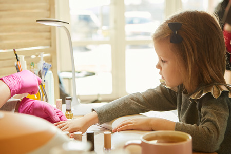 Little girl in nail salon receiving manicure by beautician. Little girl getting manicure at beauty salon.の写真素材