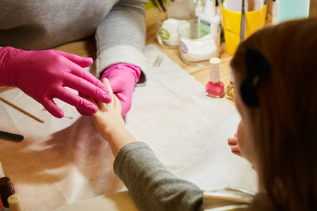 Little girl is getting manicure in beauty salon, close-up.