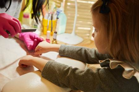 Little girl is getting manicure in beauty salon, close-up.の写真素材