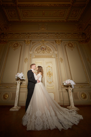 Charming wedding couple in interior in Baroque style is hugging each other on great royal palaceの写真素材