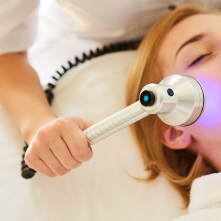 Young healthy woman with good skin doing cosmetic procedures in spa clinic. Light treatment.の写真素材