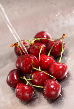 Washing sweet cherries in metal kitchen sink under water jet close-up.の写真素材