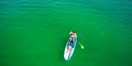 Little girl in a life vest sitting on the paddle board with mother.の写真素材