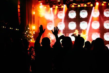 Crowd at a music concert, audience raising hands up in front of bright stage lightsの写真素材
