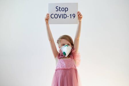 Little girl 7 years old in a medical mask is holding poster with Stop COVID-19 message. Concept 2019-nCov. Corona virus outbreaks. Epidemic virus Respiratory Syndrome. Banner for 2019 coronavirus coronavirus concept, pandemicの写真素材