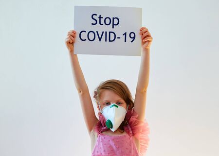 Little girl 7 years old in a medical mask is holding poster with Stop COVID-19 message. Concept 2019-nCov. Corona virus outbreaks. Epidemic virus Respiratory Syndrome. Banner for 2019 coronavirus coronavirus concept, pandemicの写真素材